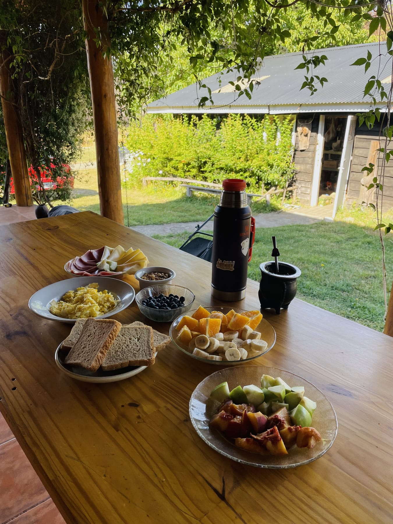 Desayuno con frutas, pan, huevos y mate en la galería