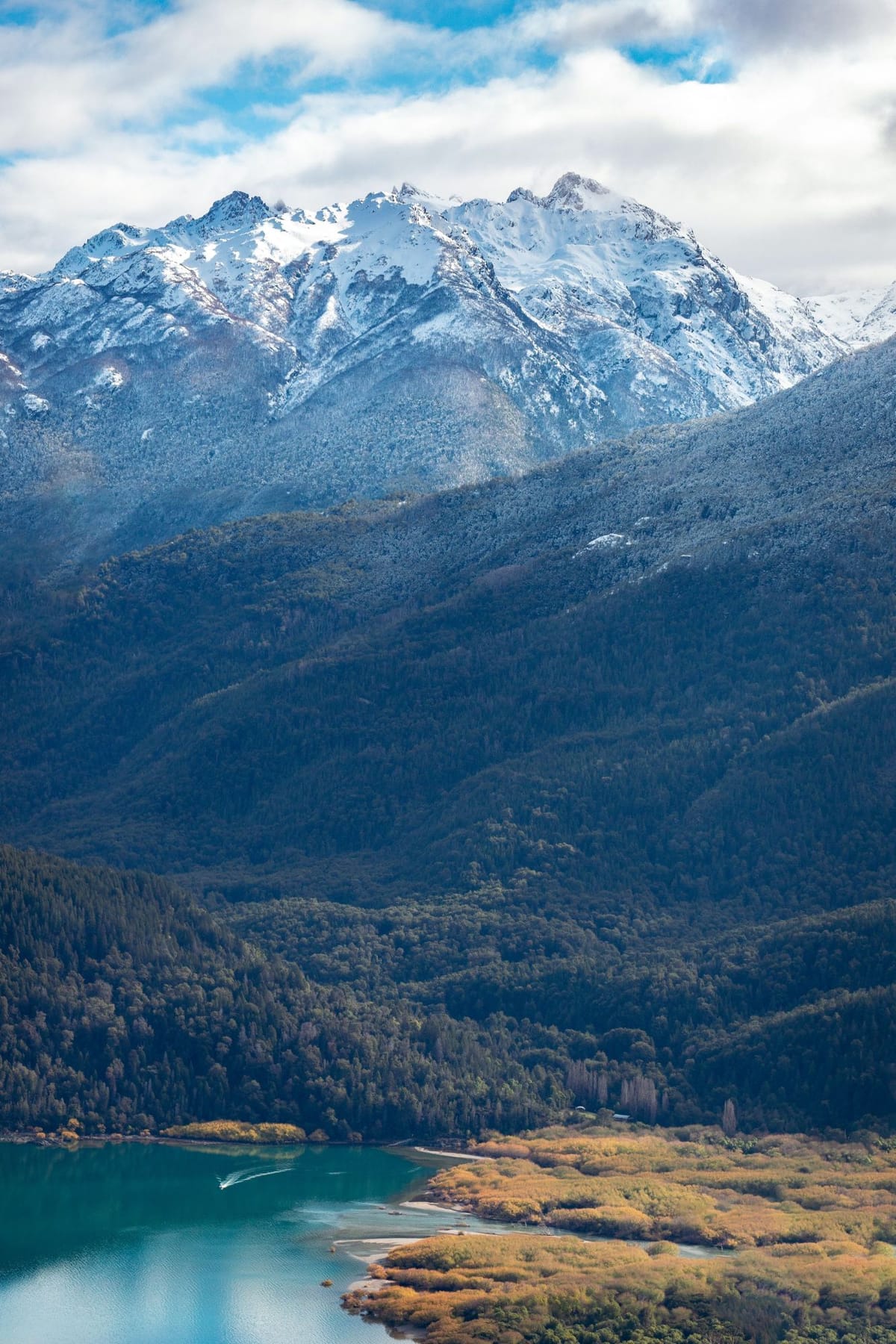 Montañas nevadas sobre el bosque y un lago turquesa con orillas doradas