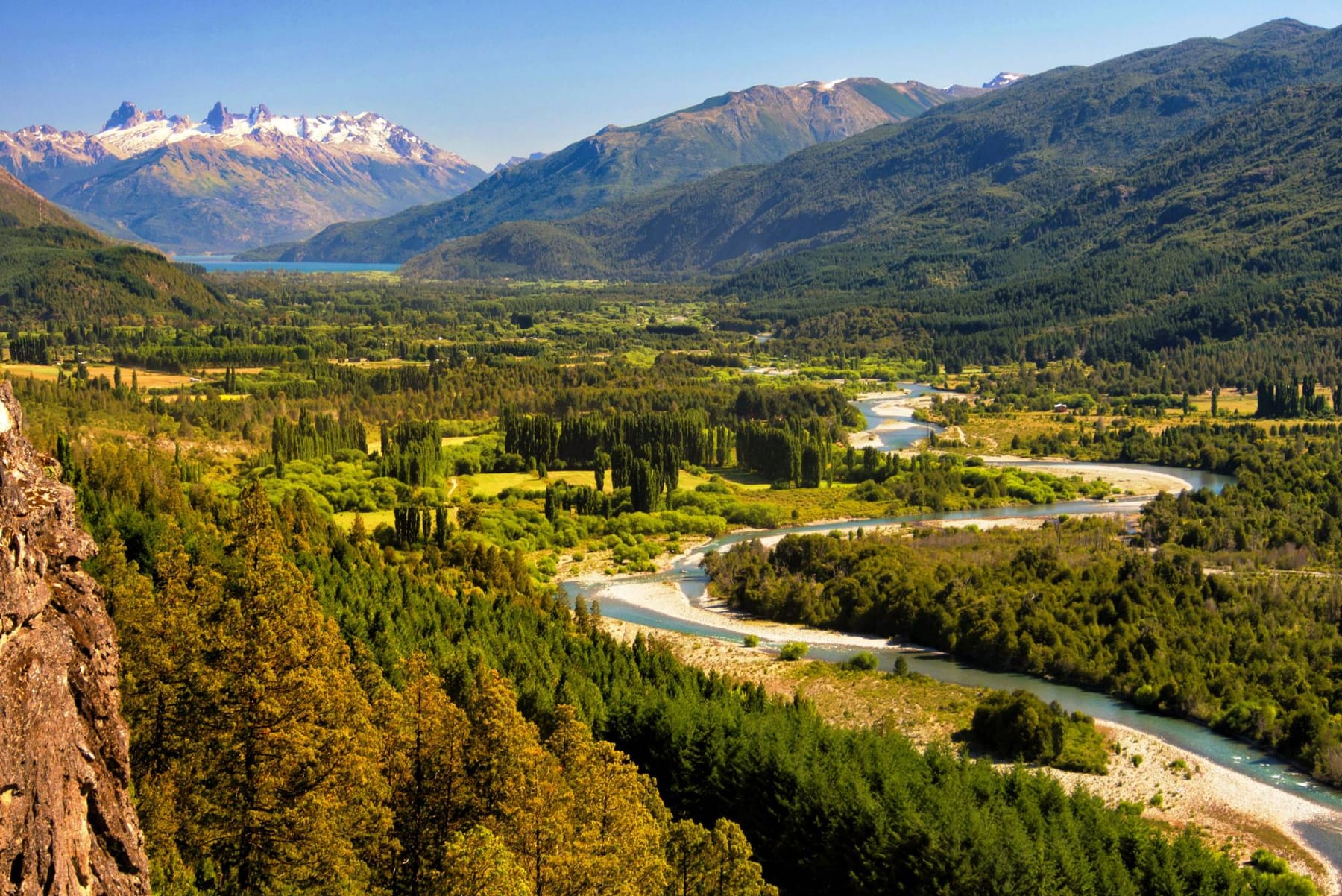 Valle verde con un río serpenteante, álamos y cerros nevados al fondo